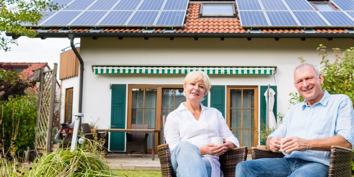 Seated older couple with solar panels on roof.jpg